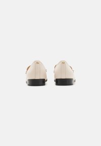 Lichtbeige leren schoenen met een lage zwarte hak, met een gladde textuur en een minimalistisch ontwerp. Geen zichtbare hardwaredetails.