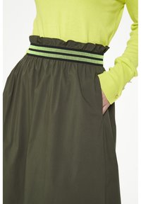 Top verde de manga larga combinado con una falda verde oscura que presenta una cinturilla con volantes, acentuada con un cinturón de rayas multicolores en contraste.