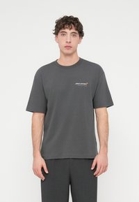 Σκούρο γκρι βαμβακερό T-shirt με κοντά μανίκια. Διαθέτει λευκό λογότυπο McLaren στην αριστερή πλευρά του στήθους. Απλός, άνετος σχεδιασμός.