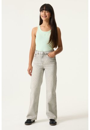 Hellgrünes, geripptes Tanktop, graue Jeans mit gepunktetem Muster, lockere Passform, Gürtel in der Taille, schwarze Turnschuhe, gerade geschnittene Hosenbeine.