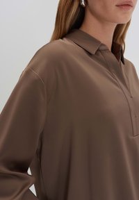 Bruine, zijden blouse met een kraag en knopenlijst. Heeft lange mouwen en een gladde textuur, ontworpen voor een ontspannen pasvorm.