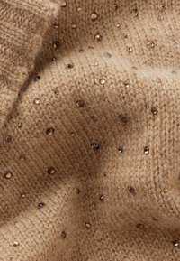 Brązowa dzianina z teksturowanym wzorem ozdobionym rozproszonymi, błyszczącymi kryształkami. Miły, przytulny wygląd.