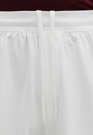 Weißer elastischer Bund mit Netzstoff und zwei langen weißen Kordeln, die herunterhängen, getragen mit einem dunkelroten Oberteil.