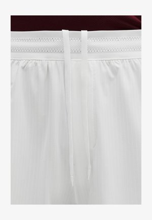 Weißer elastischer Bund mit Netzstoff und zwei langen weißen Kordeln, die herunterhängen, getragen mit einem dunkelroten Oberteil.