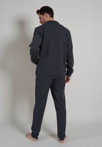 Conjunto de loungewear en gris oscuro para hombre, que incluye una camiseta de manga larga y pantalones a juego. La tela parece suave con un acabado ligeramente texturizado.
