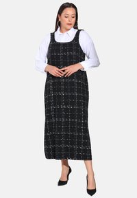 Robe à carreaux noir et blanc avec décolleté carré, sans manches, et longueur midi, réalisée en tissu texturé ; associée à des talons.