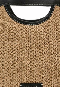 Bolso de paja trenzada con detalles en cuero negro y un asa redonda, que presenta una superficie texturizada y costuras visibles.