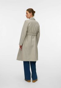 Abrigo de lana gris claro con cintura ceñida, cuello con muesca y mangas largas. Caía justo por debajo de la rodilla, combinado con pantalones de mezclilla azules.