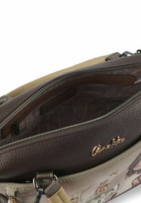 Braune Handtasche aus strukturiertem Leder mit einem hellbeigen Akzent, ausgestattet mit einer Innenreißverschlusstasche und Logodetail, die ein weiches, glattes Futter präsentiert.