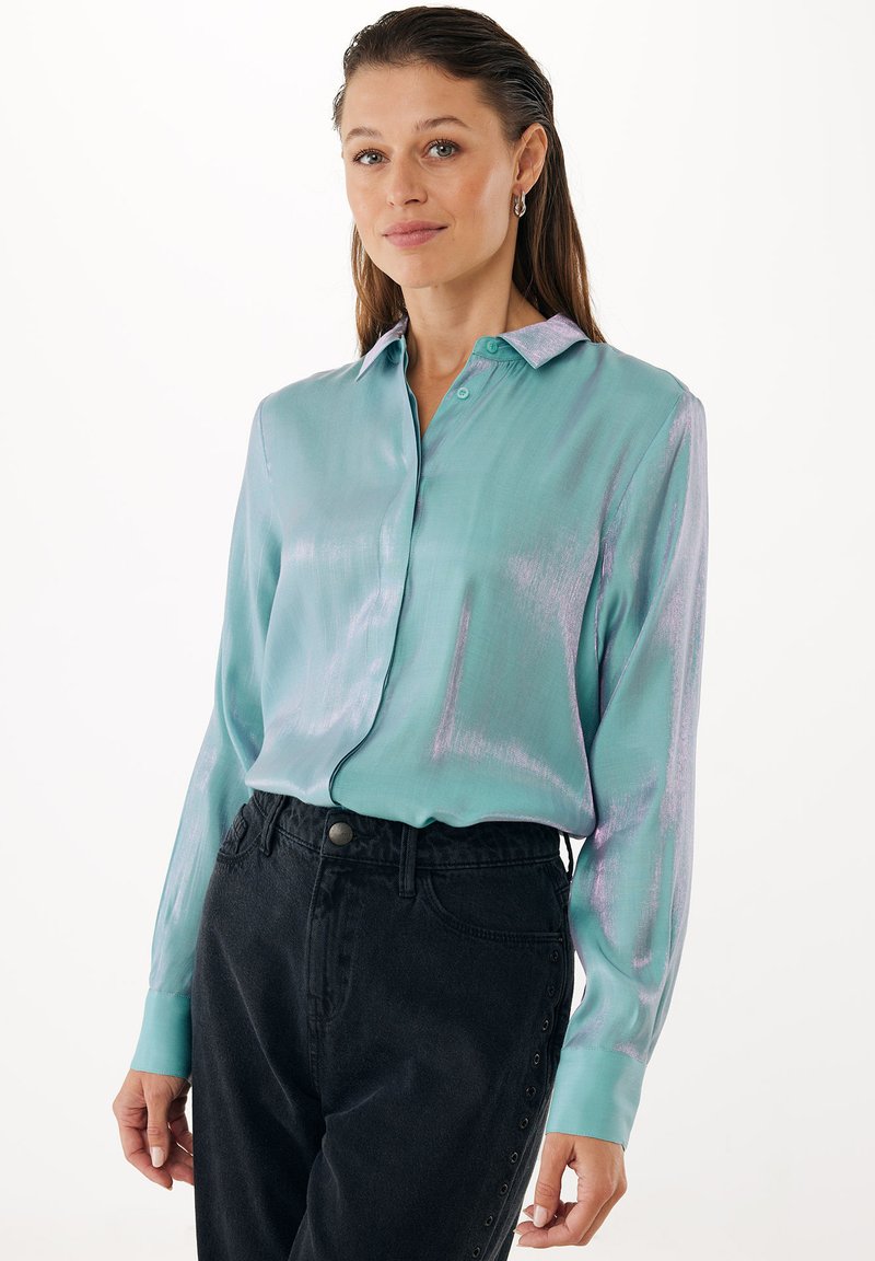 Turquoise satijnen blouse met glans, lange mouwen en een contrasterende lila kraag, gecombineerd met zwarte jeans met hoge taille.
