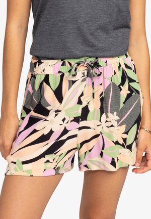 Vrouw draagt korte broek met trekkoord en bloemenpatroon in pastelroze, groen en zwart met bladeren en bloemen, gecombineerd met een donkergrijze mouwloze top.