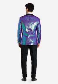 Blazer viola e verde in paillettes con una vestibilità su misura e rever neri, abbinato a pantaloni e scarpe neri, visto da dietro.
