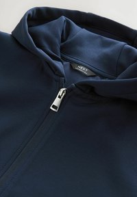Navy blue hoodie featuring a zippered front, soft fabric texture, and a lined hood with a label reading "NEXT" inside the collar.