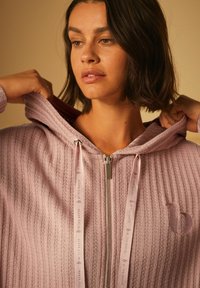 Hellblau gestreifte Zip-Hoodie mit Kapuze, verfügt über einen glänzenden silbernen Reißverschluss und gebrandete Kordeln. Texturiertes Material mit subtilen Logodetails.