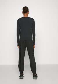 Black long-sleeve top with a round neckline, paired with black, loose-fitting jogger pants with elastic cuffs, worn with black athletic shoes.