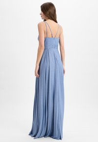 Lang, lichtblauwe jurk met een glinsterende textuur, dunne schouderbandjes en een aansluitend lijfje, met geplooide details bij de taille en een vloeiende rok.
