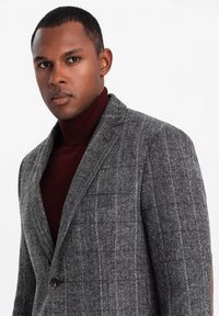 Blazer grigio a spina di pesce con un leggero motivo a quadri, chiusura a singolo bottone e rever a punta, abbinato a un maglione a collo alto bordeaux.