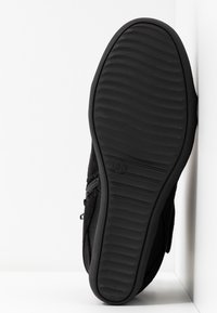 Scarpa nera con suola in gomma testurizzata, dotata di tomaia in tessuto liscio e chiusura con zip laterale. La suola presenta un motivo a onde per una maggiore aderenza.