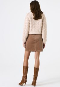 Gehaakt beige trui met golfpatroon, gecombineerd met een bruine ribstof minirok en bruine hoge laarzen met hak tot aan de knie.