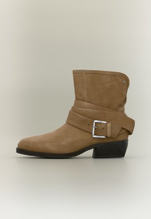 Bottine en daim marron avec design plié, bride à boucle argentée et petit talon bloc noir sur fond neutre.