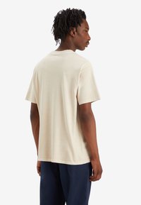T-shirt en coton beige avec une coupe décontractée, des manches courtes et un col rond, présentant une texture lisse et un design minimal.