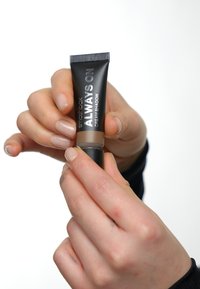 Fard à paupières crémeux Always On de Smashbox dans un petit tube noir. L'étiquette est argentée et lisible. La main tient le tube avec un vernis à ongles neutre.