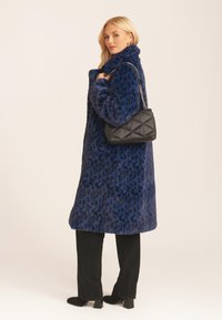 Blue leopard print faux fur coat, oversized shape, high collar, paired with a black quilted handbag. Black pants and heeled boots complete the look.