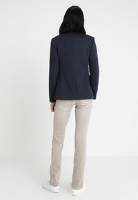 Blazer azul marino ajustado, diseño estructurado con una espalda sin costuras. Combinado con pantalones skinny gris claro y zapatillas blancas. Textura de tela suave.