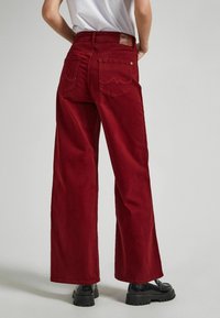 Punaiset löysät farkut, joissa on sileä pinta, kaksi takataskua ja nahkaliuska vyötäröllä. Tasainen etuosa ilman koristeita.