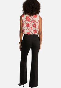 Haut sans manches floral en crème avec des motifs rouges ; associé à un pantalon noir évasé. Tissu doux, design minimaliste, sans fermetures visibles.