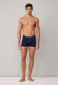 Muške bokserice tamnoplave boje s bijelim natpisom "HACKETT" na pojasu. Mekani materijal, prilagođeni kroj i duljina do sredine bedra.