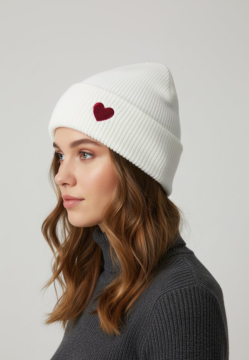 White ribbed knit beanie with a red heart patch. The beanie is snug-fitting with a fold-over brim, providing warmth and comfort.