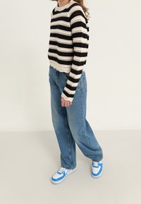 Gestreepte haaktrui in crème en zwart, gecombineerd met lichtblauwe hoge taille jeans en sneakers met blauwe accenten.
