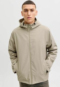 Veste beige résistante à l'eau avec une fermeture éclair à l'avant, une capuche ajustable et deux poches latérales. Texture lisse et design minimaliste.