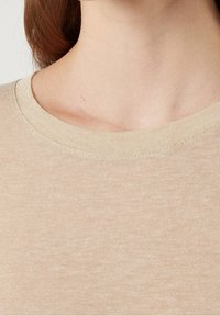 Beige kortärmad topp med rund halsringning och ett mjukt, texturerat tyg. Materialet har en diskret, lätt finish.