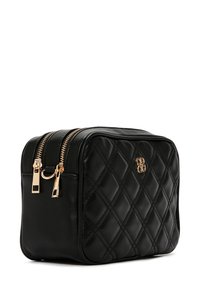 Bolso de cosméticos de cuero negro acolchado con doble cremallera dorada y un emblema de logo en la parte frontal, con una forma rectangular compacta.