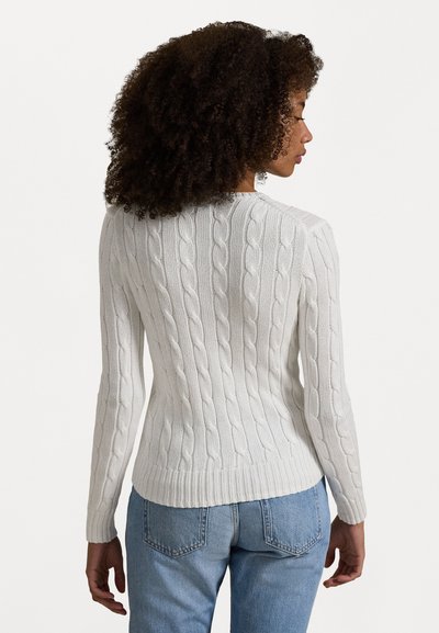 White cable-knit sweater with long sleeves and a fitted waist, featuring textured ribbing along the body. Paired with light blue jeans.