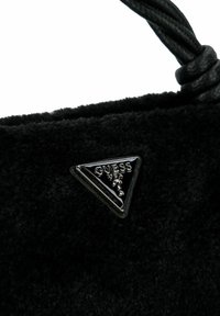 Borsa a tracolla nera in pile con superficie testurizzata, caratterizzata da un logo triangolare in metallo nero con la scritta "GUESS" in rilievo.