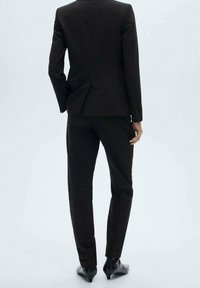 Costume noir avec une veste cintrée et un pantalon fuselé. Le tissu semble lisse avec un léger éclat. Les chaussures sont noires avec un design pointu à l'avant.