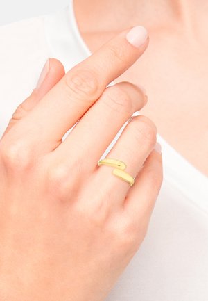 Goudkleurige verstelbare ring met twee gebogen bandsegmenten. Gladde oppervlakte met een glanzende afwerking, gedragen op een hand met een lichte huid tegen een lichte achtergrond.