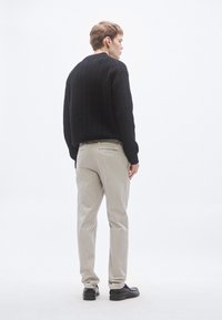 Sort strikket sweater, beige bukser, sorte sko. Sweateren har et tekstureret mønster; bukserne har en glat finish med baglommer.