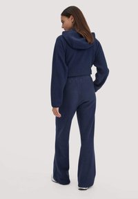 Navyblauwe fleece jumpsuit met capuchon, met lange mouwen, een getailleerde taille en flared pijpen. Zachte textuur, minimale details.