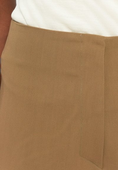 Light brown, textured fabric panel with visible stitching and a clean seam. Part of a tailored garment, possibly a pair of pants or shorts.