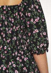 Schwarzes Blumenkleid mit kleinen weißen und pinken Blumen sowie grünen Blättern. Texturiertes Material mit elastischen Puffärmeln und Rüschensaum.