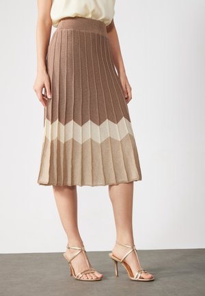 Knie-lange geplooide rok in bruine gradient met chevronpatroon, gecombineerd met beige sandalen met hoge hak en een crèmekleurige blouse.