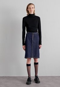 Tricou negru cu mânecă lungă și guler înalt, fustă din denim închis la culoare, cu talie înaltă, până la genunchi. Șosete negre până la genunchi cu benzi bleumarin, pantofi negri. Fundal simplu.