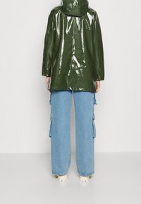 Grön glansig regnjacka med huva, bärs över vida blå denim cargo-byxor med sidofickor och avslappnad passform.