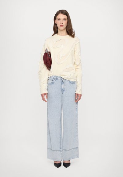 Cream knit sweater with textured cut-outs, paired with light blue wide-leg jeans. Black pointed-toe shoes and a small maroon handbag.