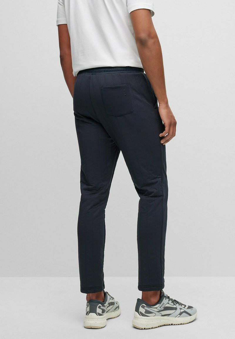 Pantalons matelassés bleu marine à coupe ajustée, dotés d'une poche arrière, d'une taille élastique et d'une texture lisse, associés à des baskets grises et noires.