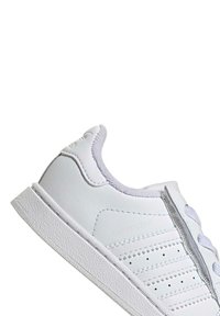 White sneaker with a smooth leather upper, textured rubber sole, three stripes design, and perforated detailing on the side.